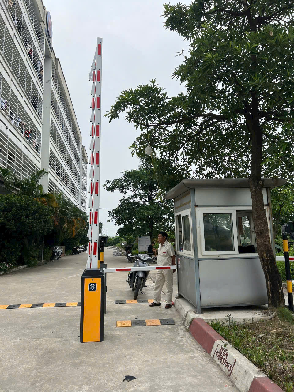 Thanh chắn barie tự động tại cổng bảo vệ tòa nhà, nhân viên bảo vệ đứng cạnh chòi gác và xe máy